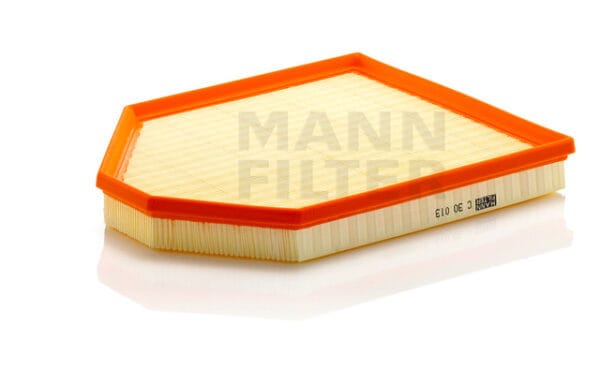 Orange and yellow automotive air filter on a reflective white surface. The words "MANN FILTER" are visible.